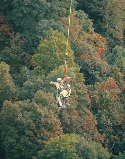 Helicopter Aerial Lift Worker Suspended Over Forested Terrain