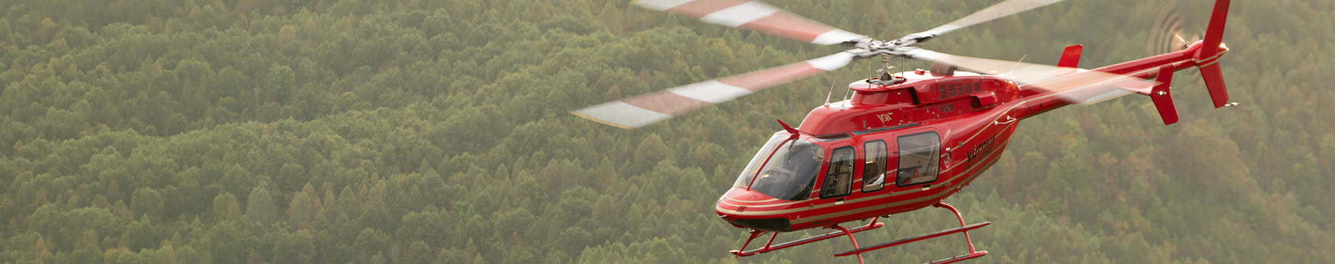 Red Emergency Medical Helicopter Flying Over Forested Mountain