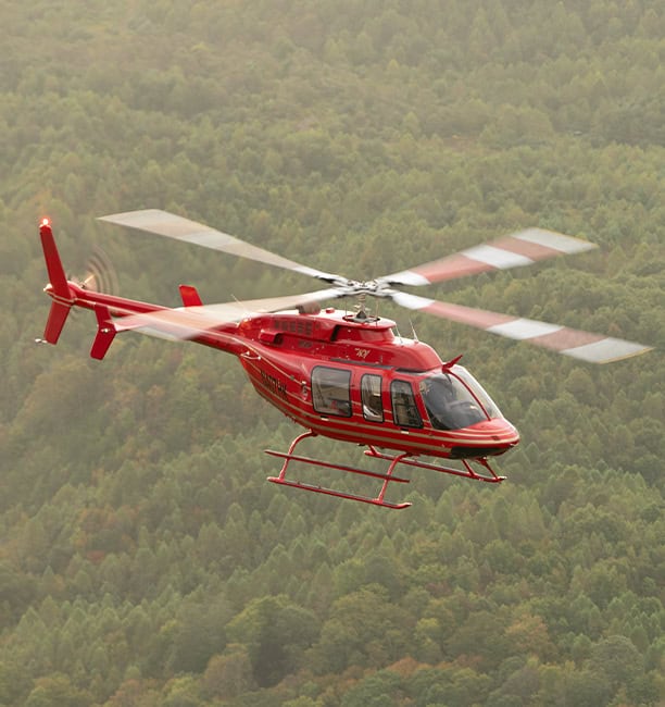 Red Utility Helicopter Flying Over Forested Mountains