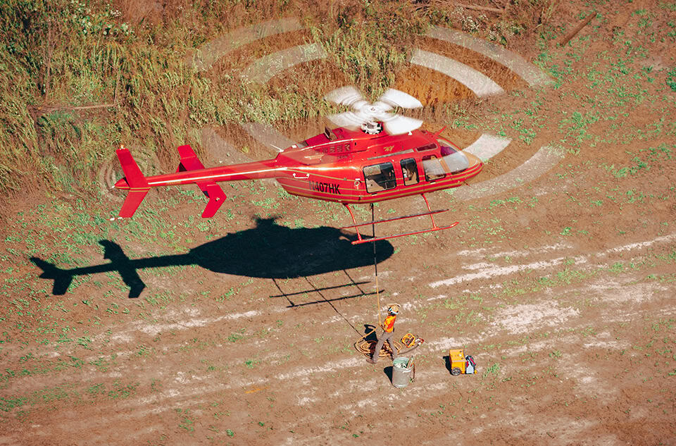 Red Utility Helicopter Performing Aerial Lift Operation With Ground Crew