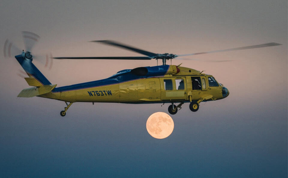 Yellow And Blue Utility Helicopter Flying At Dusk With Full Moon